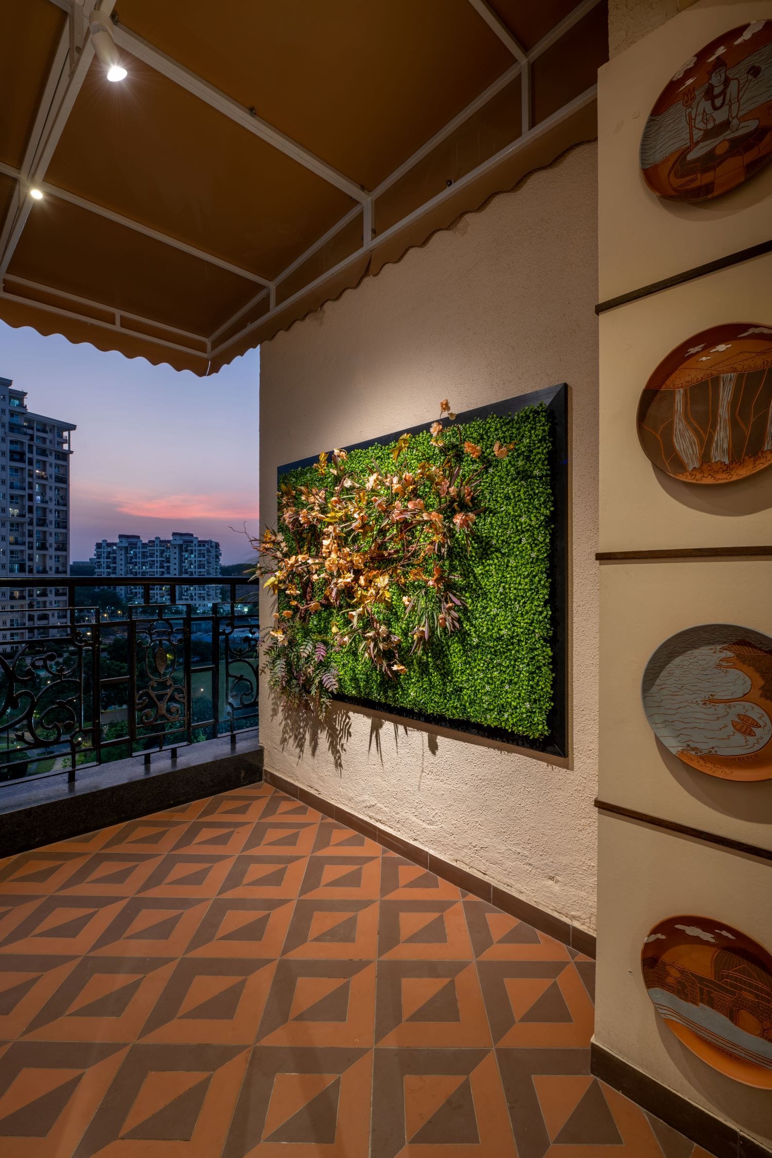 Balcony of an off-grid home designed by Metamorphic Interior Design Studio based in Pune, featuring green wall decor, geometric flooring, and artistic ceramic plates.